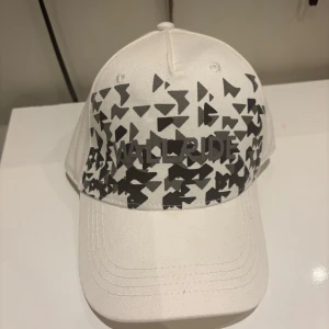 Vit keps med svart mönster Wallride - Vit keps från Wallride med coolt svart geometriskt mönster framtill och broderad logga. Justerbar rem baktill för perfekt passform. Tillverkad i bomull, perfekt för dig som vill sticka ut med en unik stil.