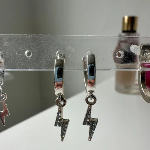 Silverörhängen med blixtar och stenar - Coola örhängen i silverfärg med hängande blixtar dekorerade med små glittrande stenar. Perfekta för dig som vill sticka ut och addera lite edge till din stil. INTE ANVÄNDA