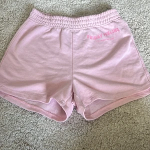 Rosa shorts med tryck 'Friday Feeling' - Mjuka ljusrosa shorts med elastisk midja och trycket 'FRIDAY FEELING' framtill. Sköna och avslappnade med klassisk sportig look, perfekta för varma dagar eller chill hemma. Tillverkade i bomull för extra komfort. Använts få gånger 