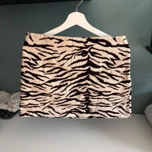 Zebramönstrad kortkjol från H&M - Snygg kortkjol från H&M med zebramönster i svart och beige. Kjolen har en rak passform och dragkedja i sidan. storlek 40 men passar även de som ör stork 38. Midjemått 38 ungefär. Aldrig använd 🥰