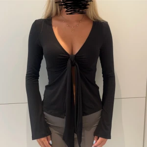 Svart topp - svart långärmad topp med djup v-ringning och knyt framtill med lätt utsvängda ärmar. Från Gina och i storlek XS💞 Använd en gång🙌🏻