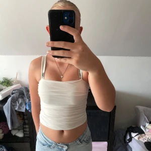 Vit croppad linnetopp Gina Tricot - Säljer en vit croppad linnetopp från Gina Tricot. Toppen har smala axelband och är figurnära med lätt rynkad effekt över magen. Perfekt till jeans eller kjol för en fräsch och enkel look.