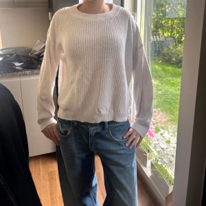 Vit stickad tröja med rund hals - Säljer en vit stickad tröja med rund halsringning och avslappnad passform. Tröjan har långa ärmar och ribbade muddar vid ärmslut och nederkant. Perfekt för lager-på-lager och enkel att matcha med jeans eller kjol.