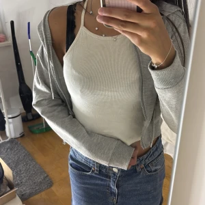 Grå croppad hoodiejacka från SHEIN - Grå croppad hoodiejacka från SHEIN i storlek XS. Jackan har dragkedja framtill, huva med snörning och ribbade muddar. Perfekt för en chill och avslappnad look. Tillverkad i mjukt och lätt syntetmaterial.