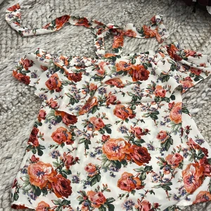 Blommig offshoulder blus  - Supersöt blus med blommigt mönster. Offshoulder-modell med volang upptill och knytband i halsen. Storlek XS-S