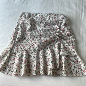 Blommig volangkjol i vitt och rosa - Supersöt kort kjol med volangkant och blommigt mönster i rosa och beige på vit botten. Tror att den är från Stradivarius men lappen är avklippt så minns inte riktigt. 