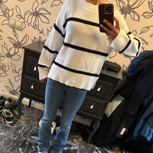  stickad tröja - Säljer en vit stickad tröja med svarta horisontella ränder. Tröjan har en avslappnad passform, rund halsringning och långa ärmar. Materialet är ribbstickat och mjukt, perfekt för lager-på-lager under kyligare dagar.