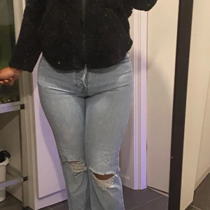 Ljusblå bootcut jeans med slitningar - Säljer ett par ljusblå jeans med bootcut passform och snygga slitningar vid knäna. Jeansen har hög midja och klassiska bakfickor. Perfekta för dig som gillar en avslappnad men trendig look.