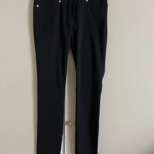 Svarta byxor från Daily Sports - Svarta byxor från Daily Sports med klassisk rak passform och diskreta silverfärgade nitar vid fickorna. Byxorna är tillverkade i ett stretchigt material som ger en bekväm känsla och snygg siluett. Perfekta för en sportig och stilren look.