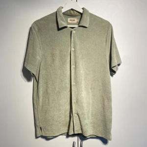 Ljusgrön frottéskjorta från East West - Snygg ljusgrön skjorta från East West i mjuk frotté. Skjortan har korta ärmar, klassisk krage och knäppning framtill med vita knappar. Perfekt för dig som gillar en chill och avslappnad stil med lite retrovibbar. Nypris 600kr. Storlek M. Välanvänd men i fint skick. 