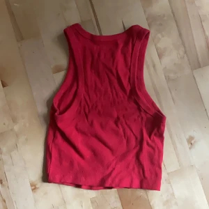 Röd ribbad linnetopp från New Yorker - Snygg röd croppad linnetopp från New Yorker i ribbad bomull. Modellen är ärmlös med breda axelband och rund halsringning. Stretchigt material men är ändå mot en mindre s modell