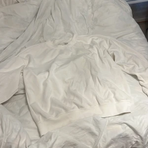 Vit basic sweatshirt i bomull - Enkel och stilren vit sweatshirt med rund hals och långa ärmar. Tröjan är i mjuk bomull och har en relaxed passform som passar perfekt till jeans eller mjukisbyxor. Ribbad mudd vid ärmslut och nederkant för en klassisk look.