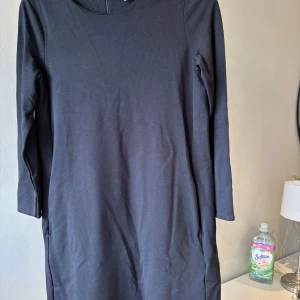 Svart enkel klänning från H&M - Svart, stilren klänning från H&M Basic med lång ärm och rund halsringning. Modellen är rak och kort, med dragkedja bak. Perfekt för dig som gillar minimalistisk och clean stil.