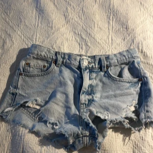 Ljusblå jeansshorts från Gina Tricot - Snygga ljusblå jeansshorts från Gina Tricot med råa, slitna kanter och trasiga detaljer. Klassisk femficksmodell med knapp och dragkedja framtill. Perfekta för sommardagar när du vill ha en avslappnad och trendig look. De var favoritshortsen förra sommaren men är tyvärr för små nu