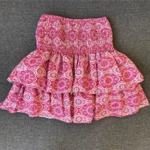 Rosa volangkjol från Meet x Tiger - Supersöt kort volangkjol från Meet x Tiger i rosa med paisleyinspirerat mönster. Kjolen har bred smock i midjan och dubbla volanger som ger en fluffig och lekfull look. Perfekt att styla med sneakers eller boots för en chill vibe.