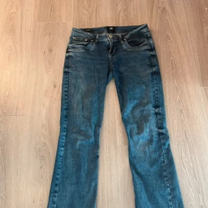 Blå bootcut jeans från LTB 27/30 - Snygga blå jeans från LTB med klassisk femficksdesign och bootcut-ben. Jeansen har låg midja och är tillverkade i ett mjukt denimtyg med lätt slitna detaljer och kontrastsömmar. Perfekta för dig som gillar en avslappnad men ändå trendig look.
