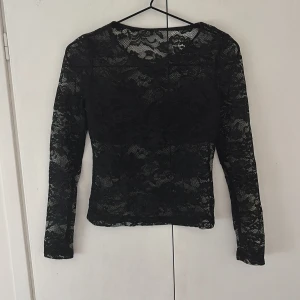 Svart spetstopp - Säljer en svart spetstopp som är perfekt att ha till fest. Toppen har en tight passform och är tillverkad i ett stretchigt spetsmaterial.
