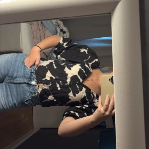 Svart och vit blus med knappar - Säljer en svart och vit blus med abstrakt mönster och korta puffärmar. Blusen har knappar framtill och en lätt v-ringning. Perfekt att styla med jeans eller kjol.