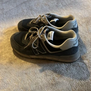 New balance skor - Säljer ett par klassiska mörkblåa New Balance sneakers med grå detaljer och vita loggor på hälen. Skorna har snörning och en robust, mönstrad sula som ger bra grepp. Perfekta för en avslappnad och sportig stil. Skriv om ni har frågor!