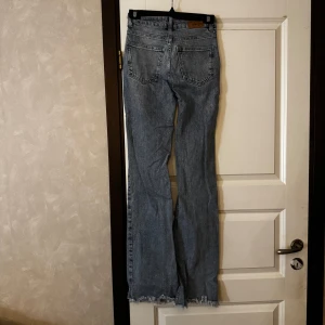Ljus blåa bootcut jeans med råa kanter - Säljer ett par ljus blåa bootcut jeans med råa, fransiga benslut. Jeansen har fem fickor och normal passform upptill. Perfekta för dig som gillar en retrostil med lite extra vidd nedtill.