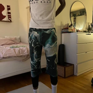 Grönmönstrade shorts  - Säljer ett par unika shorts med grön och vit mönster. De har normal passform och går ner till knäna. Perfekta för dig som vill sticka ut med en cool och modern stil.