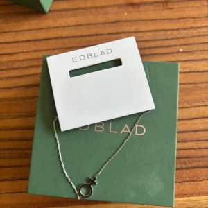 Silverfärgat halsband från Edblad med kvinnosymbol - Säljer ett stilrent silverfärgat armband från Edblad med en kvinnosymbol som hänge. Kedjan är tunn och elegant, perfekt för att lyfta din look med en subtil detalj. Levereras i originalförpackning.