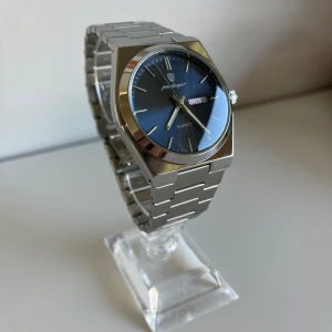 Silverfärgad klocka från Poedagar - Stilren klocka från Poedagar med blå urtavla och dag/datumvisning. Armband är i silverfärgad metall med klassisk länkdesign. Quartz-urverk och tydliga indexmarkeringar.
