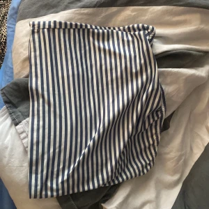 Blåvit randig kortkjol - Säljer en blåvit randig kortkjol med klassiskt mönster. Kjolen har en rak passform och är perfekt för varmare dagar. Enkel och stilren design som passar till många olika toppar.