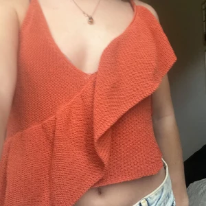 Orange/korall stickad linnetopp från Zara - Säljer en orange stickad linnetopp från Zara med volangdetalj framtill. Toppen har smala axelband och v-ringning, perfekt för varma dagar. Snygg och trendig modell som passar till mycket.