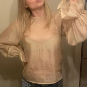 Beige blus med vida ärmar - Säljer en beige blus med långa, vida ärmar och resår vid ärmsluten. Blusen är tillverkad i ett tunt, lätt material och har en enkel rund halsringning. 
