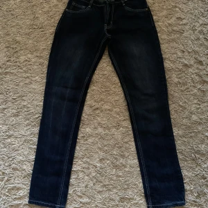 Mörkblå jeansbyxor från Bonito Jeans - Snygga mörkblå jeansbyxor från Bonito Jeans med klassisk femficksdesign och kontrastsömmar. Byxorna har rak passform och normal midja, perfekta till vardags. Tydlig logga på bakfickan och knappstängning framtill.