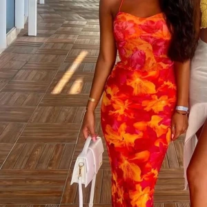 Färgstark blommig långklänning med smala axelband - Säljer en snygg långklänning med smala axelband och figurnära passform. Klänningen har ett färgstarkt blommigt mönster i rött, orange och gult. Perfekt för sommarens alla tillfällen!