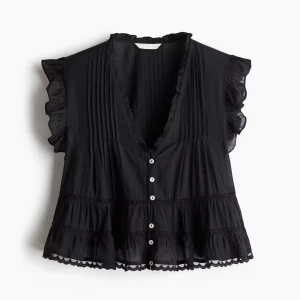 Svart blus med volangdetaljer - Supersöt svart blus med volang vid ärmar och nederkant, djup v-ringning och knappar framtill. Tunt och luftigt material med fina spetsdetaljer längs kanterna. Perfekt för att lyfta vilken outfit som helst!