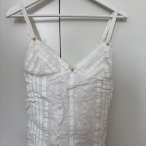 Vit spetsdetaljerad linnetopp/blus från Zara  - Säljer en söt vit linnetopp från Zara med tunna axelband och spetsdetaljer. Toppen har broderade mönster och en lätt v-ringning framtill. Perfekt för varma dagar eller som ett lager under en skjorta.
