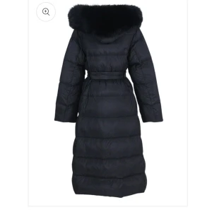 Svart lång dunjacka med pälskrage och bälte - Snygg svart lång dunjacka med stor pälskrage och bälte i midjan. Jackan har en quiltad design och långa ärmar, perfekt för kalla dagar. Ger en elegant och lyxig känsla till vinterlooken.