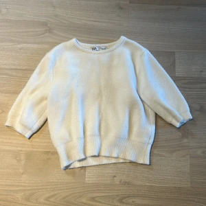 Vit stickad tröja från Zara - Mysig vit stickad tröja från Zara med rund halsringning och trekvartsärmar. Tröjan har ribbade muddar vid ärmslut och nederkant, perfekt för en stilren och enkel look.