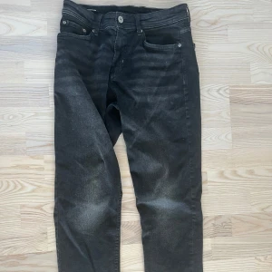 Svarta jeansbyxor från Lefties - Säljer ett par svarta jeansbyxor från Leftiesman i modellen Comfort Slim. Byxorna har klassisk femficksdesign, knappgylf och diskreta slitningar för en cool look. Perfekta för dig som gillar en smalare passform men ändå vill ha komfort.