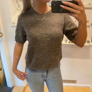 Brun stickad tröja från Gina Tricot - Mysig brun stickad tröja från Gina Tricot med korta ärmar och rund halsringning. Perfekt att matcha med jeans eller kjol för en enkel och stilren look.