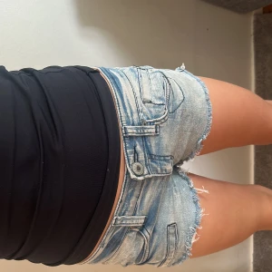 Ljusblå jeansshorts från Western - Säljer ett par ljusblå jeansshorts från Western Newyork med fransade benslut och klassiska fem fickor. Shortsen har låg midja och slitna detaljer för en avslappnad look. Perfekta för varma dagar och enkel att matcha med olika toppar. Står att dom är i M men skulle säga Xs