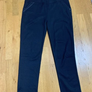 Svarta stretchiga byxor med fickor - Säljer ett par svarta byxor med stretchigt material och bekväm midja. Byxorna har snedställda fickor framtill med knappdetalj och en bakficka. Perfekta för en stilren och enkel look.