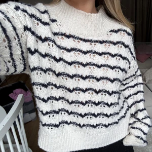 Vit stickad tröja med svarta ränder från Neo Noir - Säljer en vit stickad tröja från Neo Noir med svarta vågiga ränder och hålmönster. Tröjan har rund halsringning och långa ärmar. 