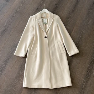 Cremefärgad vit kappa från H&M ny med prislapp  - Stilren beige kappa från H&M med klassisk krage och en knapp framtill. Aldrig använd.