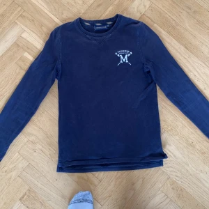 Mörkblå långärmad tröja från Morris R. Club - Säljer en mörkblå långärmad tröja från Morris R. Club med broderad logga på bröstet. Tröjan har rund halsringning och klassisk passform. Perfekt för en stilren och avslappnad look. Och det går att diskutera pris 