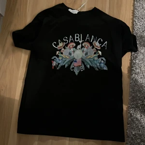 Svart t-shirt från Casablanca - Snygg svart t-shirt från Casablanca med ett färgglatt tryck på framsidan. Perfekt för en avslappnad stil med en touch av lyx. Passar bra till jeans eller shorts för en cool look.