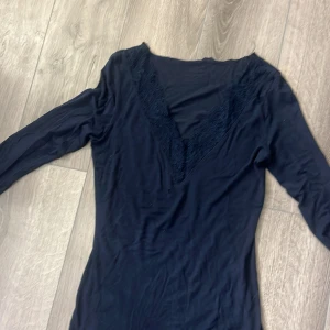 Marin blå  långärmad topp med spetsdetaljer - Snygg marin blå långärmad topp med v-ringning och spetsdetaljer runt halsen. Perfekt för en stilren look. Toppen är gjord i ett mjukt material som känns skönt mot huden.två hål ett vid magen och ett vid armen 
