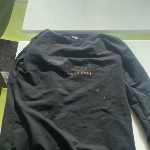 Svart långärmad tröja från Hugo Boss - Säljer en stilren svart långärmad tröja från Hugo Boss. Tröjan har en diskret logga i orange på bröstet och är perfekt för en avslappnad men ändå elegant look.