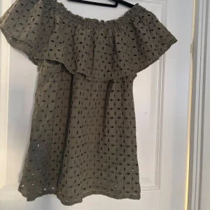 Olivgrön offshoulder blus från Part Two - Säljer en olivgrön offshoulder blus från Part Two med ett vackert broderat mönster. Blusen har en volangdetalj runt axlarna och är perfekt för en somrig look. Den är tillverkad i ett lätt och luftigt material.