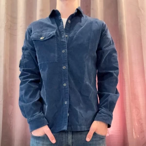 Blå overshirt från C.P. Company - Snygg blå overshirt från C.P. Company med Manchester tyg, med långa ärmar och knappar framtill. Skjortan har en unik detalj på ärmen och en bröstficka med knapp. Perfekt för en stilren look. Helt ny!! Org pris 3299.