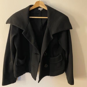 Svart kappa från Lindex - Elegant svart kappa från Lindex med stora knappar och bred krage. Perfekt nu inför våren . Det står storlek L, men är liten i storleken och passar mig som brukar ha xs-s