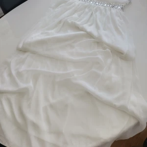 Vit klänning från Donna Bella - Elegant vit klänning från Donna Bella i SIDEN blandning med glittriga detaljer runt midjan och bysten. Klänningen har axelband och en luftig design som ger en fin passform. Perfekt för speciella tillfällen. Klänningen är helt ny! 16 (GB) dvs ca 40 - 42 (M)